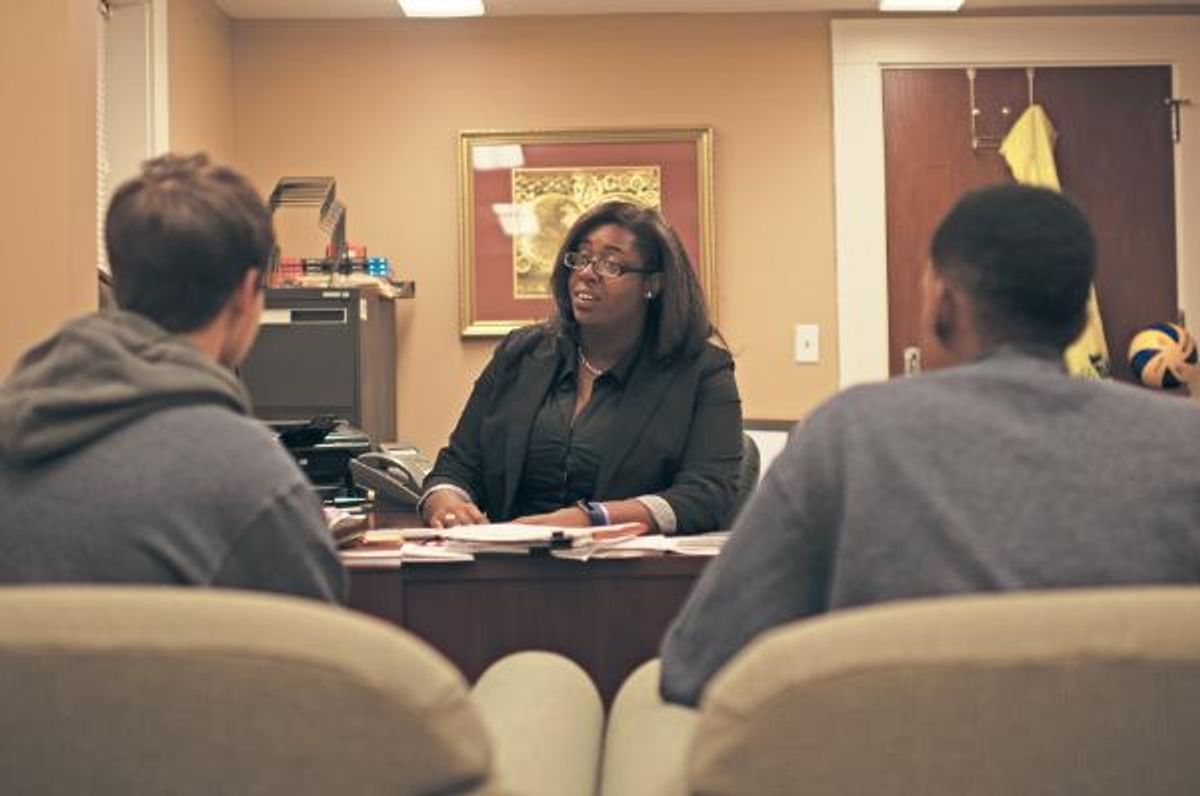 Latoya sits at desk and talks with two students