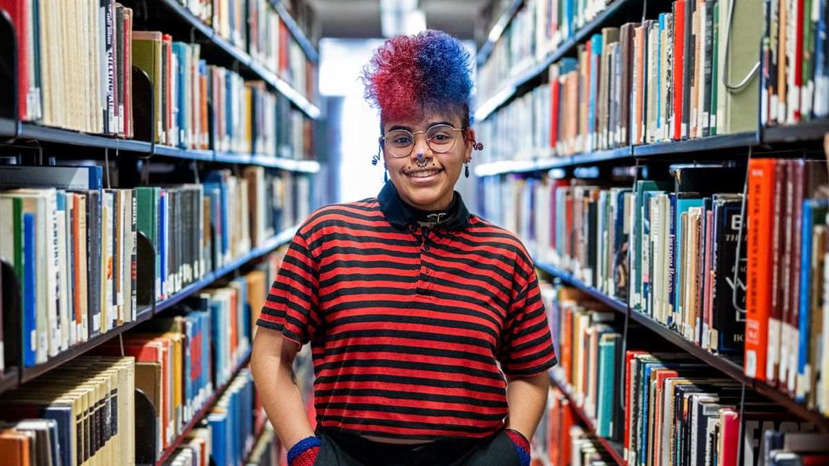 Kol Tavares standing in the library with their hands in their pockets.
