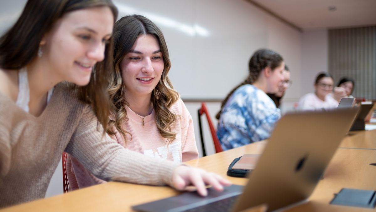 Two female students looking at a laptop while in class