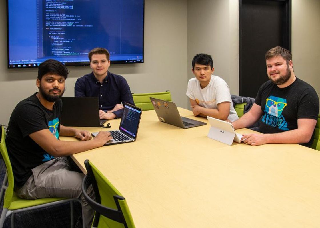 Four students sitting around a table with their laptops