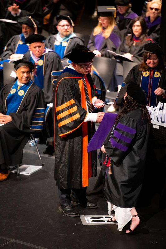 Students receive their scroll, hood, and diplomas