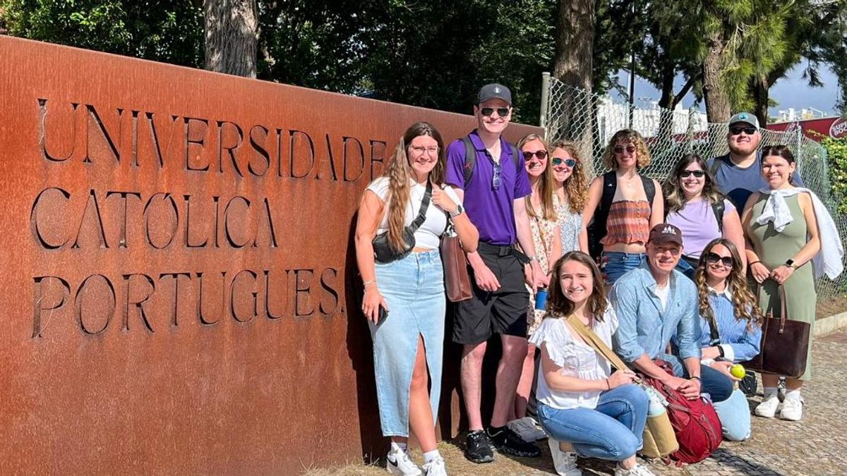 Ten UMass Law students and Professor Richard Peltz-Steele pose by the Universidade Católica Portugues campus logo.