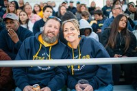 A cheerful couple sits close together in the stands at Cressy Field for the Blue & Gold Weekend football game