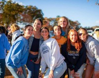 A group of seven young women are smiling and posing together during Blue & Gold Weekend