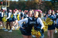 Two Corsair cheerleaders with gold and blue pom-poms pose and smile at the football game with a group of cheerleaders in the background wearing matching uniforms and pink bows