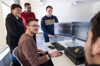Business students and Associate Dean Chan Du gather around a Bloomberg Terminal in the Charlton Technology Center