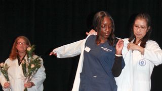 Student assisted in her white coat by nursing professor
