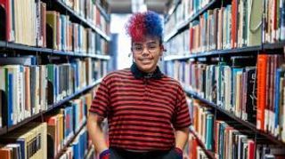 Kol Tavares standing in the library with their hands in their pockets.