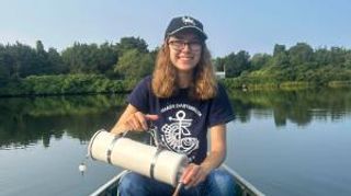 Mia Oliveira '26 sitting on a boat smiling while holding research equipment