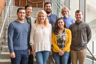Winning team of five students and two faculty mentors standing on the stairs in Claire T. Carney Library