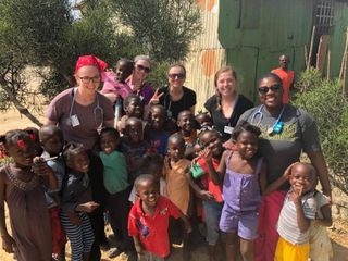 Casual photo of a large group of young children with College of Nursing students in bright sunshine in Haiti.