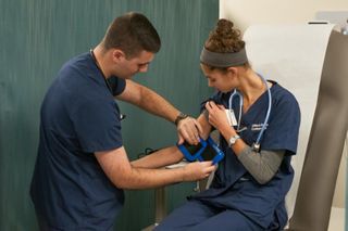 Male nursing student practicing taking blood pressure on a female nursing student