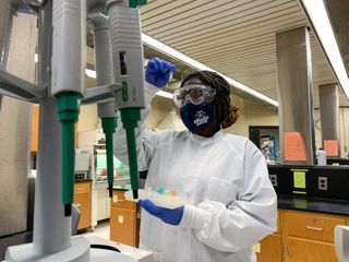 student in lab safety gear examining specimen