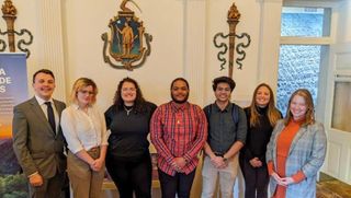 UMassD students Brad Ferris, Kelly Grodecki, Patrice Strague, Parker Sowersby, and Taha Bin Amer with [names] at [place] celebrating the launch of their app prototype.