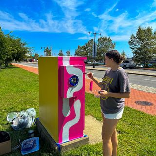 Illustration student Chloe Canterbury paints an electrical box alongside Route 18