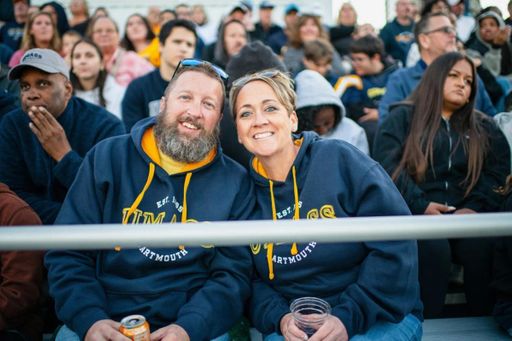 A cheerful couple sits close together in the stands at Cressy Field for the Blue & Gold Weekend football game