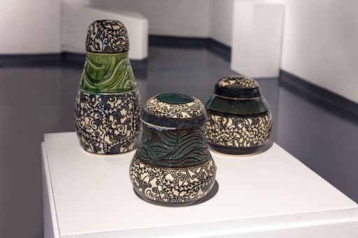 Subconscious Sgraffito, 2023, two short green jars with round lids and a combination of carved markings as well as detailed designs with a tall jar with a round cap lid that also has a combination of carving and designs, 13 x 6 ½ in, 6 ½ x 7 in, 7 ½ x 7 ½ in.