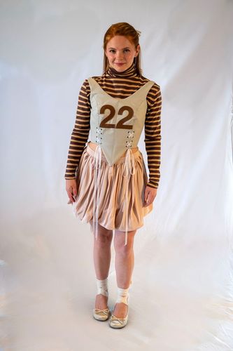 Look 1, 2026, pink flowy bubble skirt with leather lace up corset featuring a leather “22” and striped turtleneck top underneath.