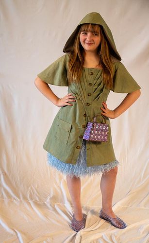 Look 3, 2026, green army dress with pleated bodice, exaggerated flutter sleeves, hood, army pockets and button placket, paired with a blue shag skirt, and a pink vinyl box purse.