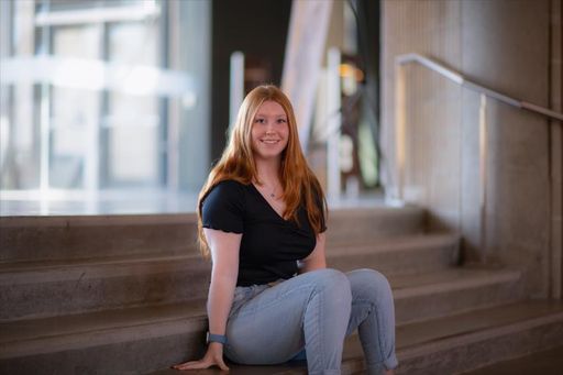 Paige Riley '23, nursing major and Spanish minor, sits on the stairs of the Claire T. Carney Library