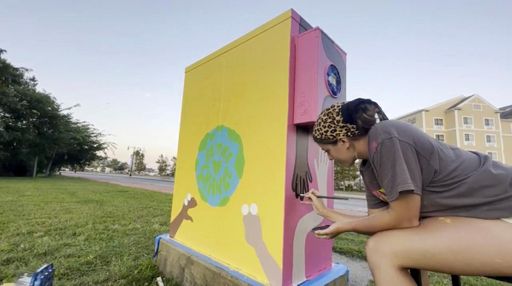 Illustration student Chloe Canterbury paints an electrical box alongside Route 18