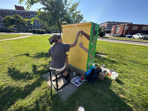 Illustration student Chloe Canterbury paints an electrical box alongside Route 18.