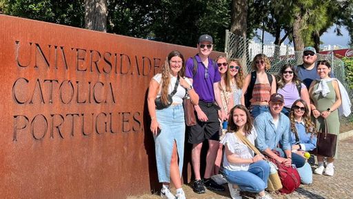 Ten UMass Law students and Professor Richard Peltz-Steele pose by the Universidade Católica Portugues campus logo.