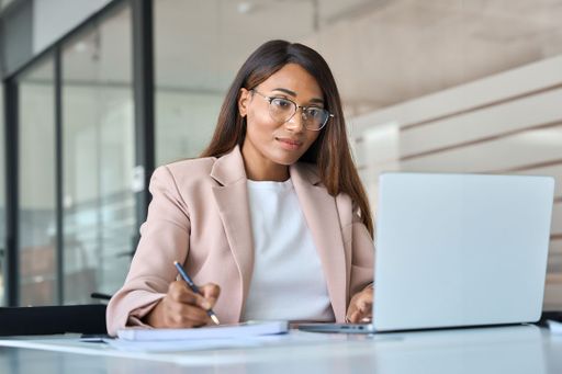 Woman at her desk taking notes while on her computer