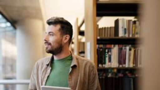 Male student holding digital tablet looking away from the camera.