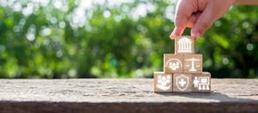 Hand stacking wooden blocks with icons symbolizing social policy elements like healthcare, justice, and community support.