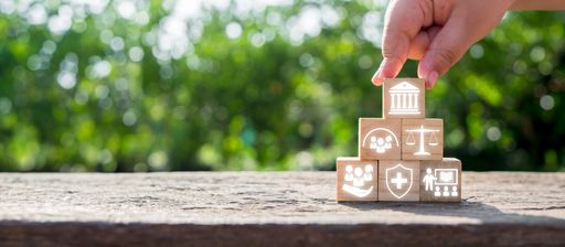 Hand stacking wooden blocks with icons symbolizing social policy elements like healthcare, justice, and community support.