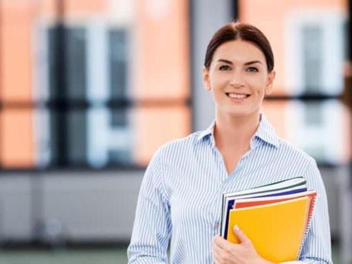 brunette teacher holding folders and notebooks while standing in school corridor