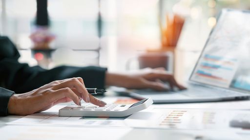 Closeup of hands using a calculator and laptop