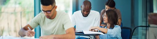 Female school professor helping a male student in a lecture hall while student is taking an exam on paper..