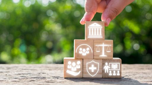 Hand stacking wooden blocks with icons symbolizing social policy elements like healthcare, justice, and community support.