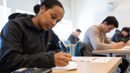 Student sitting at a desk with a pencil, paper, and calculator.