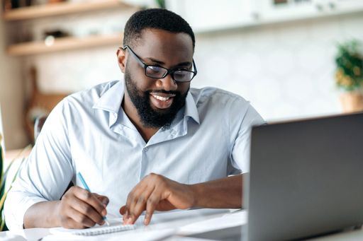 Friendly successful confident african american bearded male with glasses, broker, taking notes, distant learning, smiling