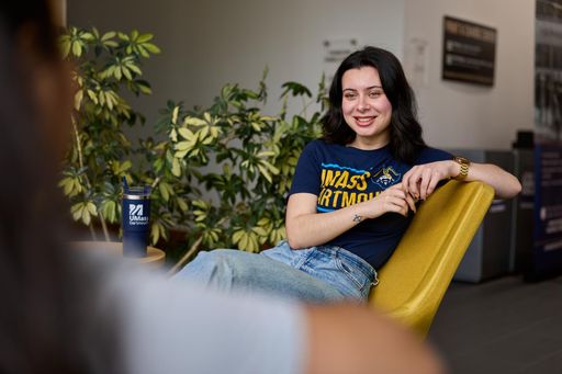 Student relaxed in a chair wearing UMass Dartmouth apparel.