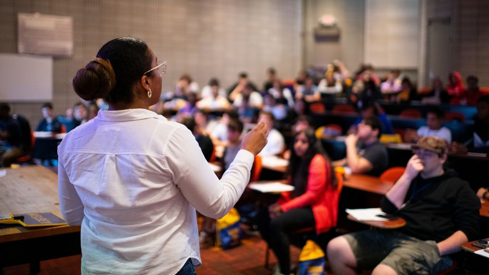 A lecturer standing in front of students in a lecture hall.
